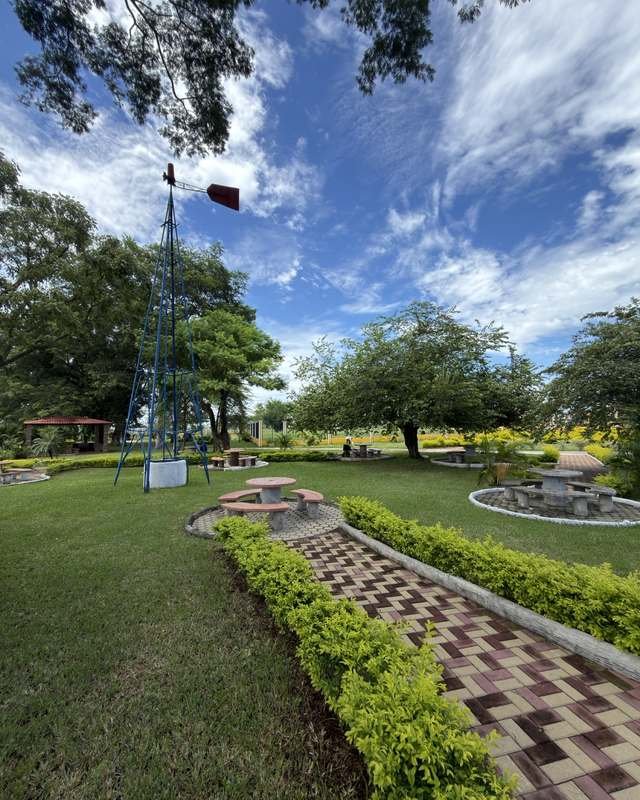 Mesas de concreto, caminamientos de adoquín y molino azul entre árboles en Palmeras Sur