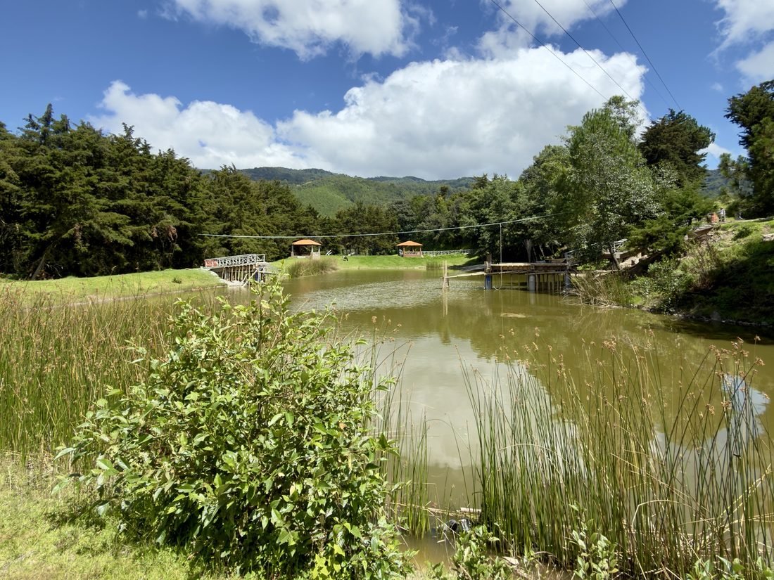 Vista completa de la laguna de Buenaventura Tecpán, con sus puentes de madera y los cerros al fondo